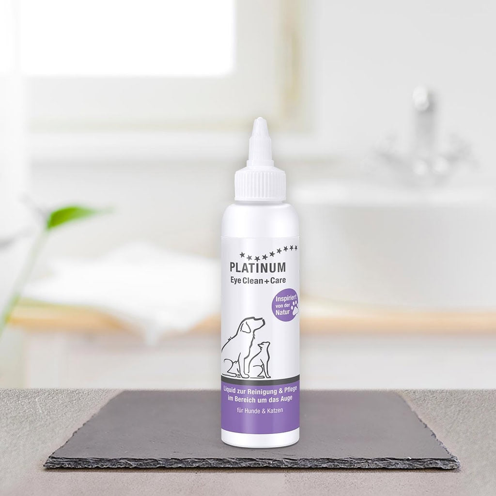 Bela steklenička PLATINUM Eye Clean + Care, Nega Oči za Pse in Mačke stoji na temni ploščici v svetli kopalnici, v ozadju sta zamegljena umivalnik in brisača.