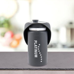 Siv Prenosni bidon z lijakom za pse blagovne znamke PLATINUM z belimi zvezdicami in prostornino 550 ml leži na temni površini z zamegljenim kuhinjskim ozadjem.