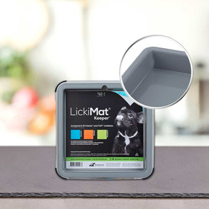 PLATINUM LickiMat® - BUDDY KEEPER, siv kvadratni držalo za LickiMat, je razstavljen na pultu. Na njegovi embalaži so prikazani črn pes, podrobnosti o izdelku in približek vogala - idealen za uporabo s katero koli podlogo za lizanje LickiMat.