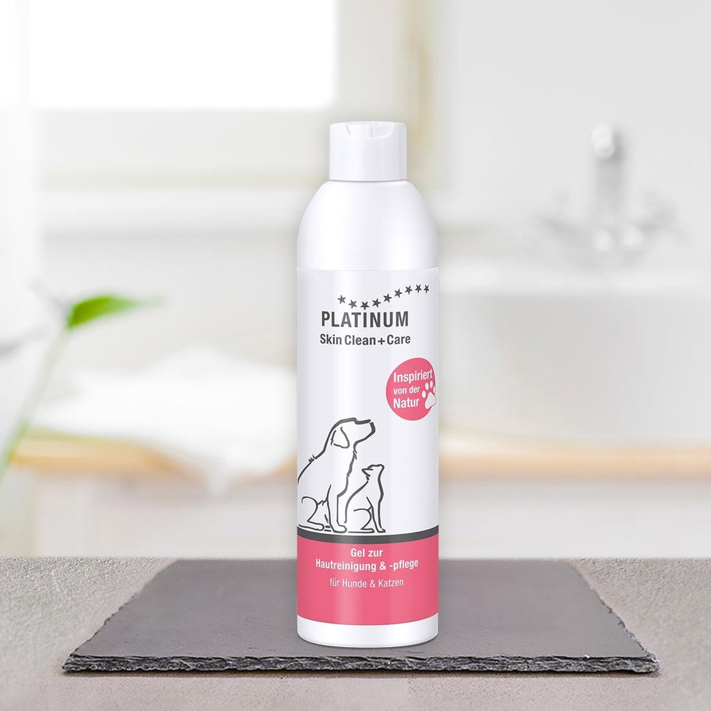 Bela steklenička PLATINUM Skin Clean + Care, Nega Kože za Pse in Mačke s podobo psa in mačke stoji na temni površini v svetli, zamegljeni kopalnici-odličen za naravno nego srbeče kože pri psih in mačkah.