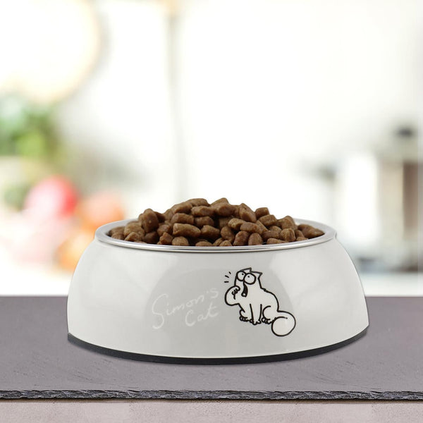 PLATINUM Posoda za hrano in pijačo Simon's Cat, napolnjena s suho mačjo hrano, stoji na pultu. Na beli posodi je črna linijska risba Simonove mačke in besedilo. Ozadje je mehko zamegljeno.